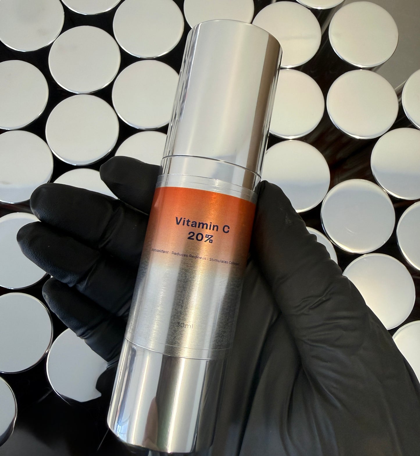 Hand holding a skincare serum bottle labeled 'Vitamin C 20%' against a patterned background.